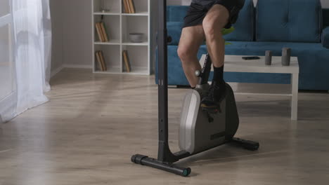 sporty-man-is-spinning-pedals-of-exercise-bike-at-home-details-view-training-and-keeping-his-physical-condition-sport-and-activity